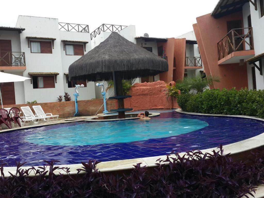 a large swimming pool with an umbrella in a courtyard at Flat Recanto dos Golfinhos in Pipa