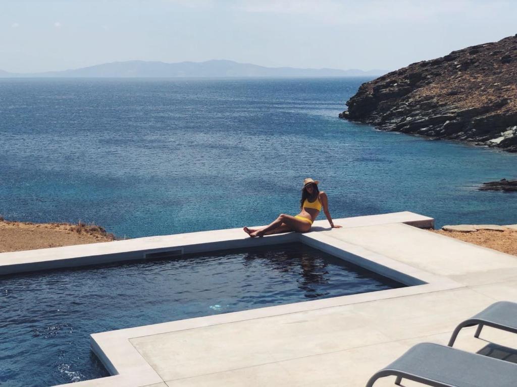 una mujer sentada en el borde de una piscina con vistas al océano en Archipelagotinos, en Agios Romanos