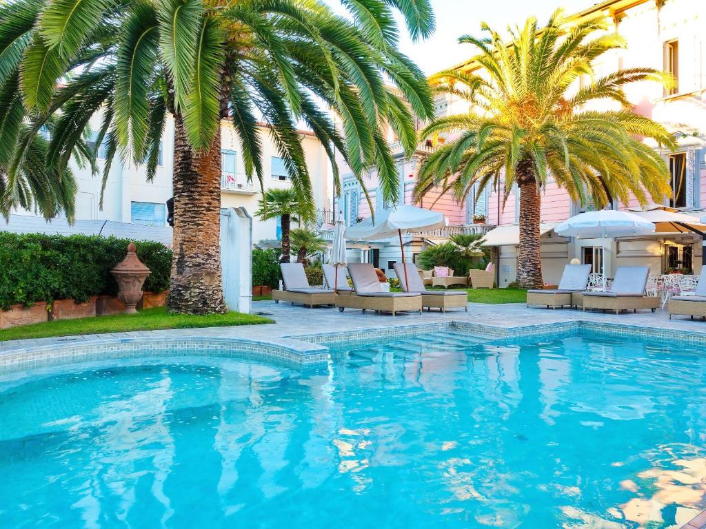 a pool with palm trees and chairs and a building at Hotel Europa in Lido di Camaiore