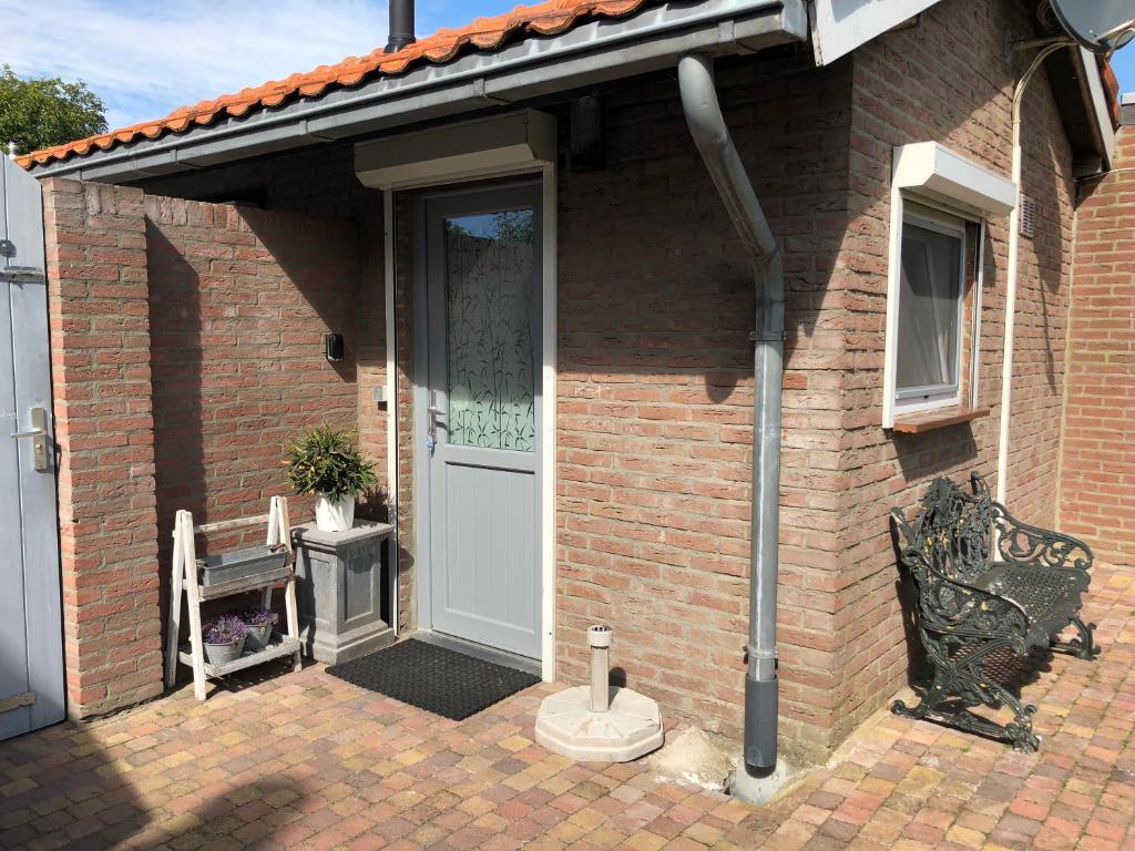 a brick house with a white door and a bench at Slapen bij de Zeeuwse Lala in IJzendijke