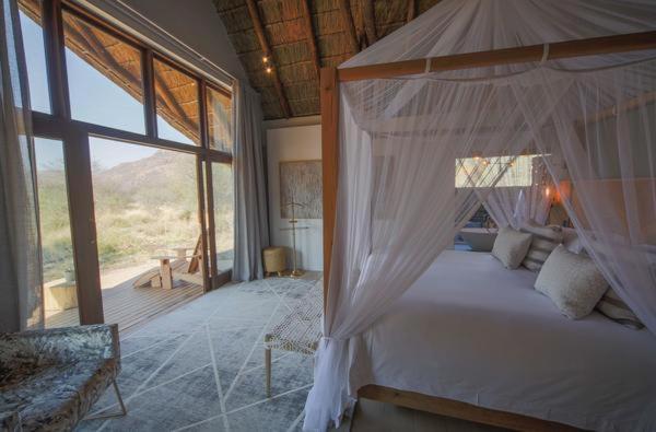 ein Schlafzimmer mit einem Himmelbett und einem großen Fenster in der Unterkunft Nkala Safari Lodge in Matlhagame