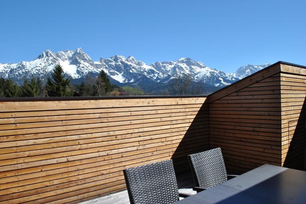two chairs and a table on a wooden fence with snow covered mountains at Der Winklhof in Saalfelden am Steinernen Meer