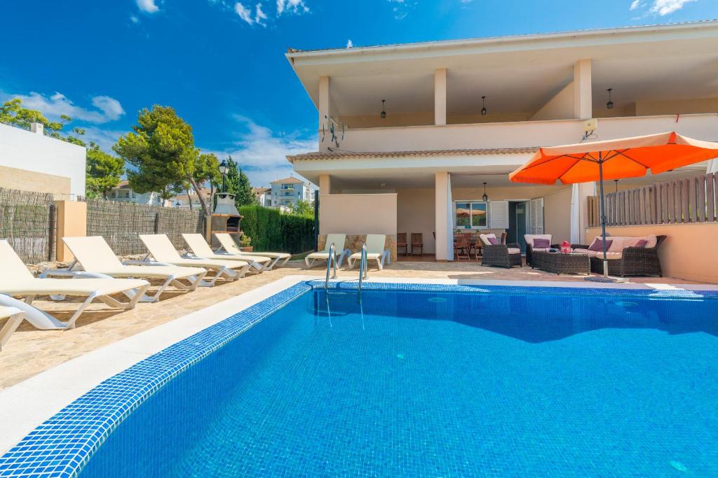 a swimming pool in front of a house with an orange umbrella at Villa JERONIMO Alcudia in Muro