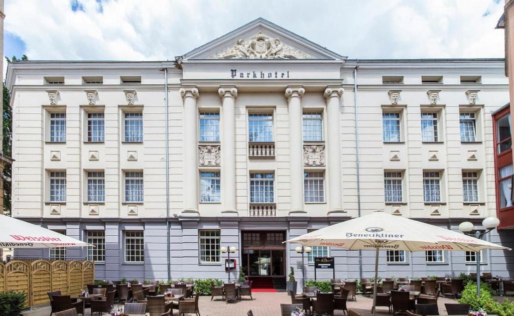 a large white building with tables and umbrellas at Parkhotel Altenburg in Altenburg
