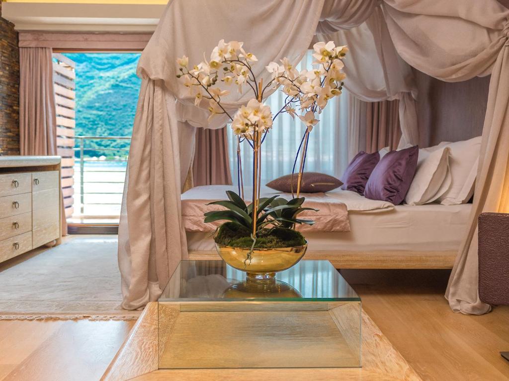a vase with flowers on a glass table in a bedroom at Hotel Forza Mare in Kotor