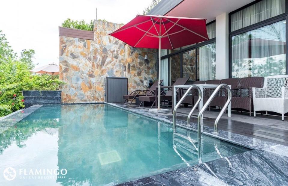 uma piscina com um guarda-sol vermelho e cadeiras e uma mesa em Flamingo Villa Happy BT em Ngọc Quang