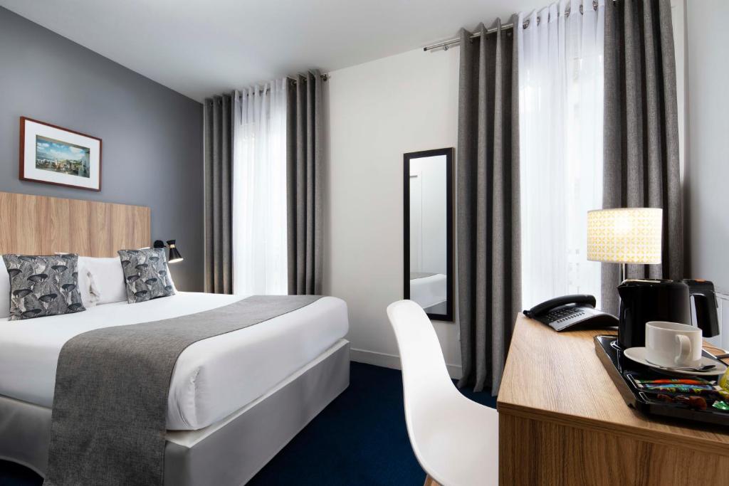 パリにあるムーラン ヴェールのベッドとデスクが備わるホテルルームです。