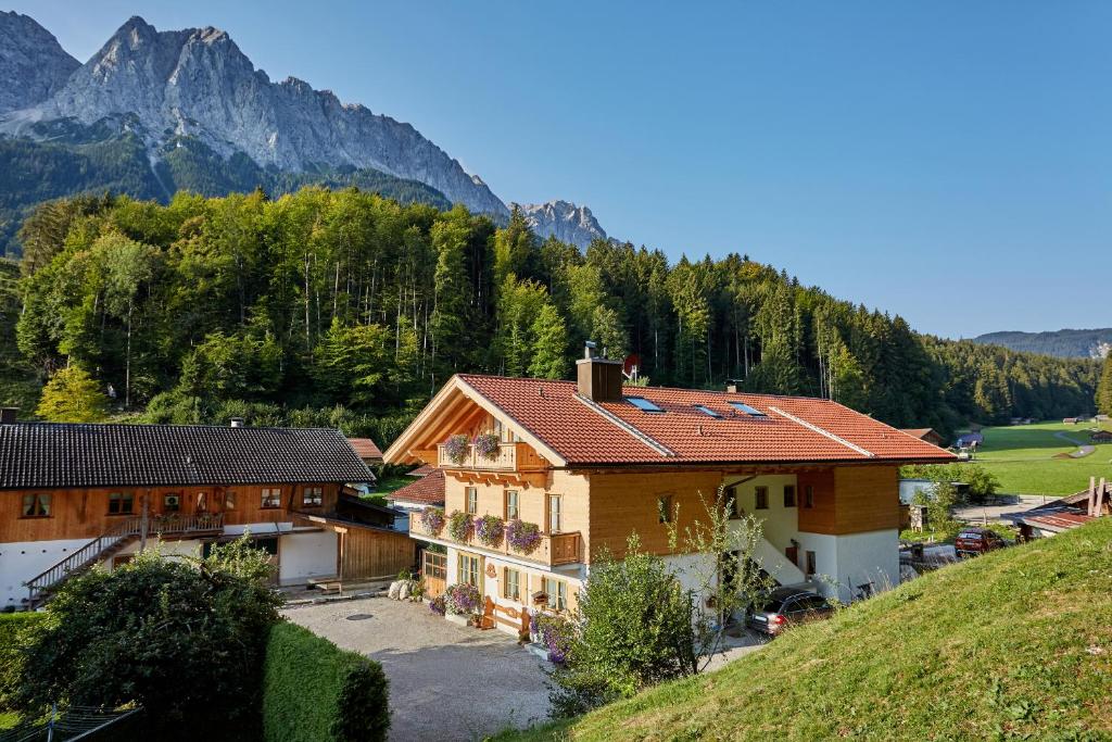 una casa en una colina con montañas en el fondo en Ferienwohnungen Pfanzelter, en Grainau