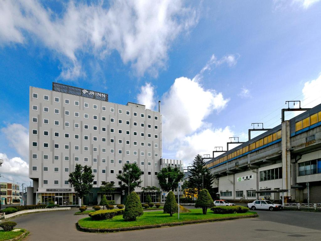 un gran edificio blanco con un coche aparcado en un aparcamiento en JR Inn Chitose en Chitose