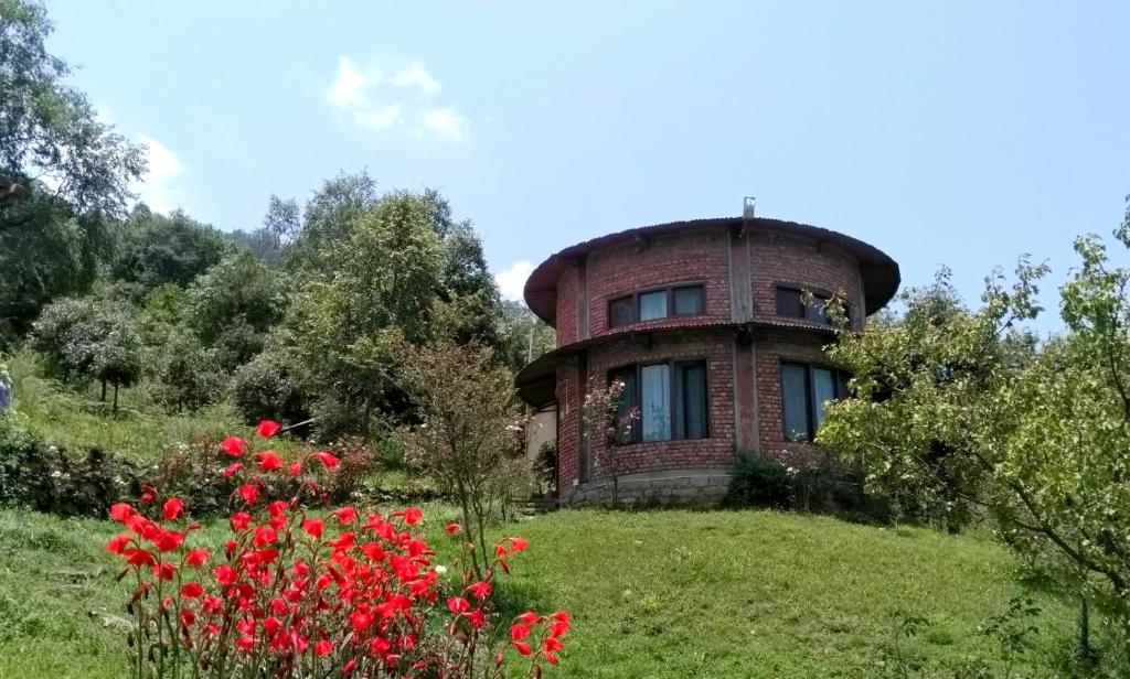 uma casa redonda numa colina com flores vermelhas em The Misty Mountains em Chaukori