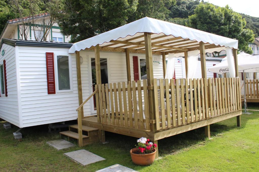 a small white house with a wooden deck at Camping Playa Arenillas in Islares