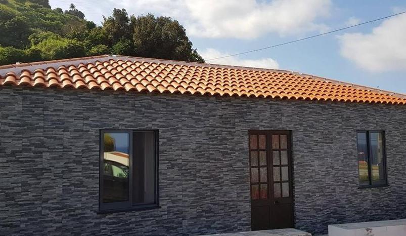 a brick house with a red roof and two windows at Casa da Cruz in Santa Cruz das Flores