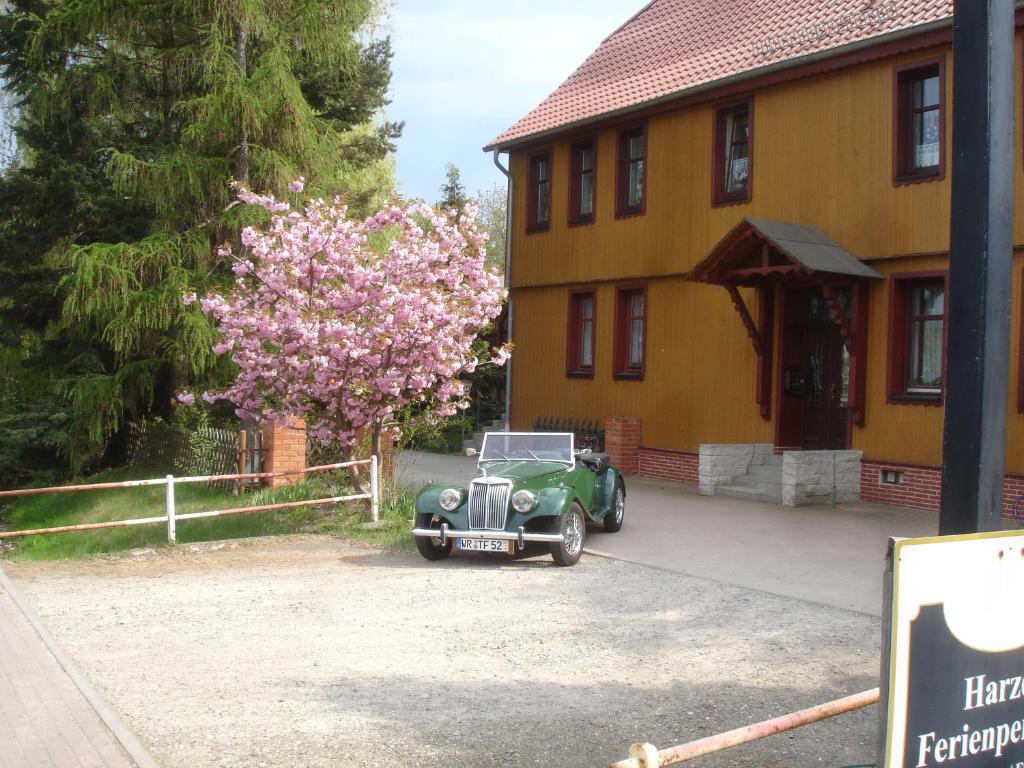 une voiture verte garée devant une maison avec un arbre à fleurs dans l'établissement Harzer Ferienpension, à Timmenrode