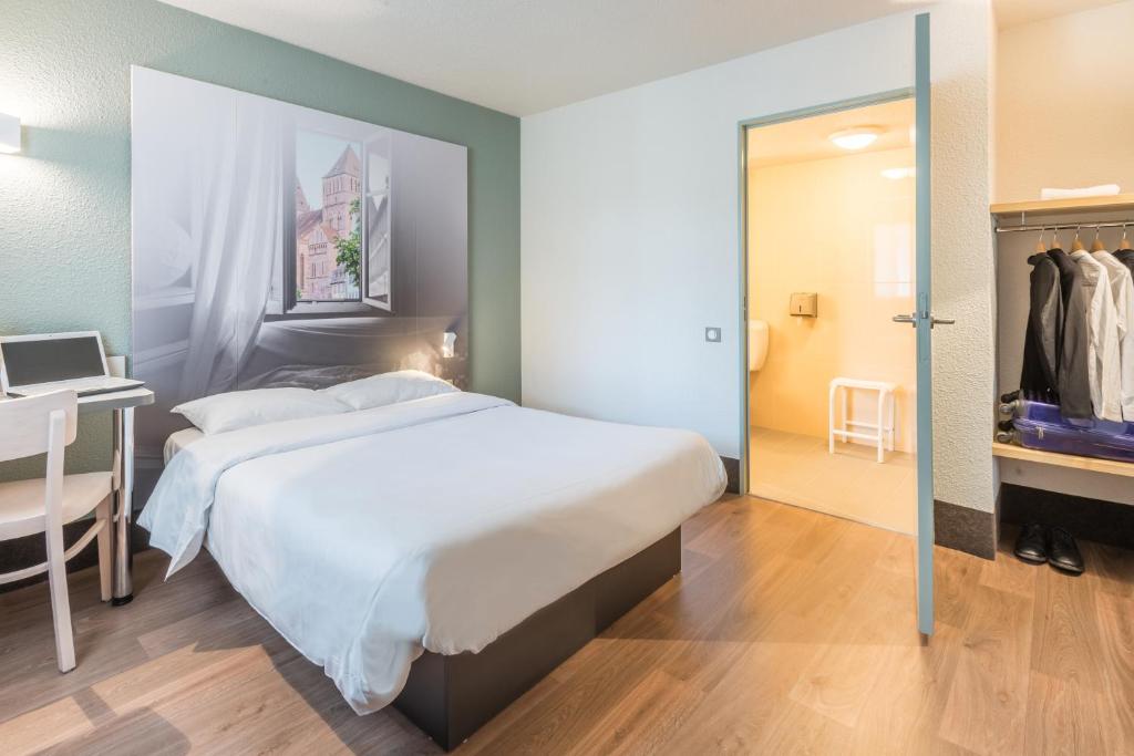 a bedroom with a bed and a desk and a mirror at B&B HOTEL Paris Le Bourget in Le Bourget