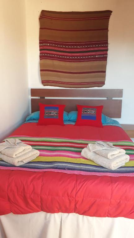 Una cama roja con almohadas rojas y toallas. en Hostal Open House en San Pedro de Atacama