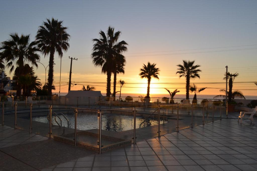 a pool with palm trees and a sunset in the background at Playa Paraíso Resort in Concón