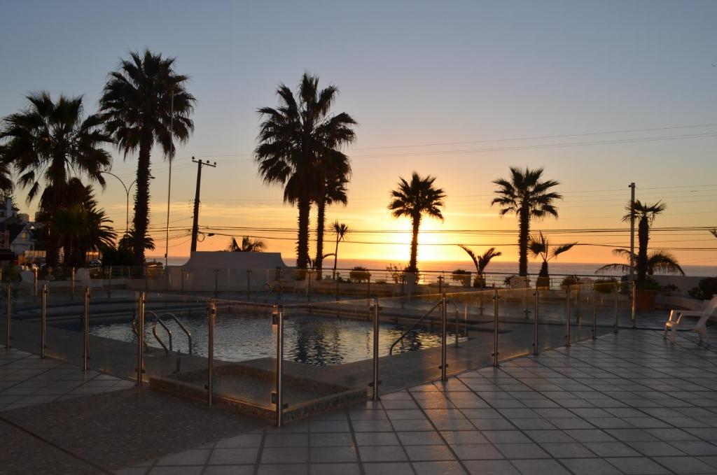 una piscina con palmeras y una puesta de sol en el fondo en Playa Paraíso Resort, en Concón