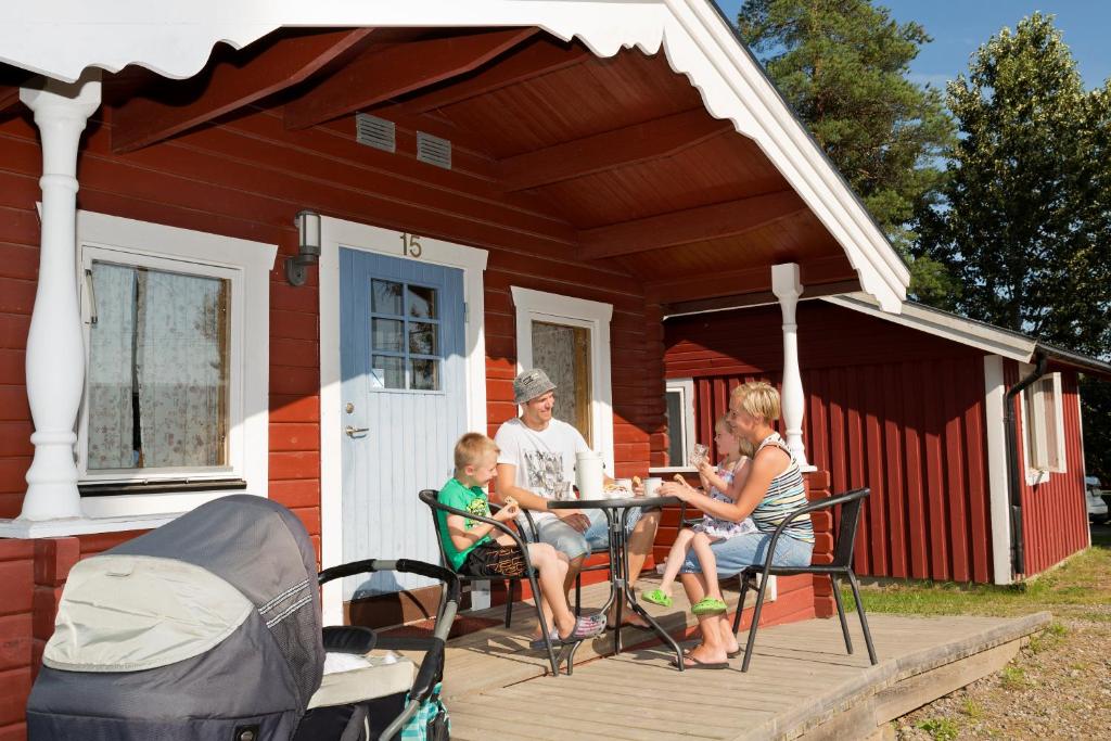 a family sitting at a table on the porch of a red house at Vännäs bad & camping in Vännäs