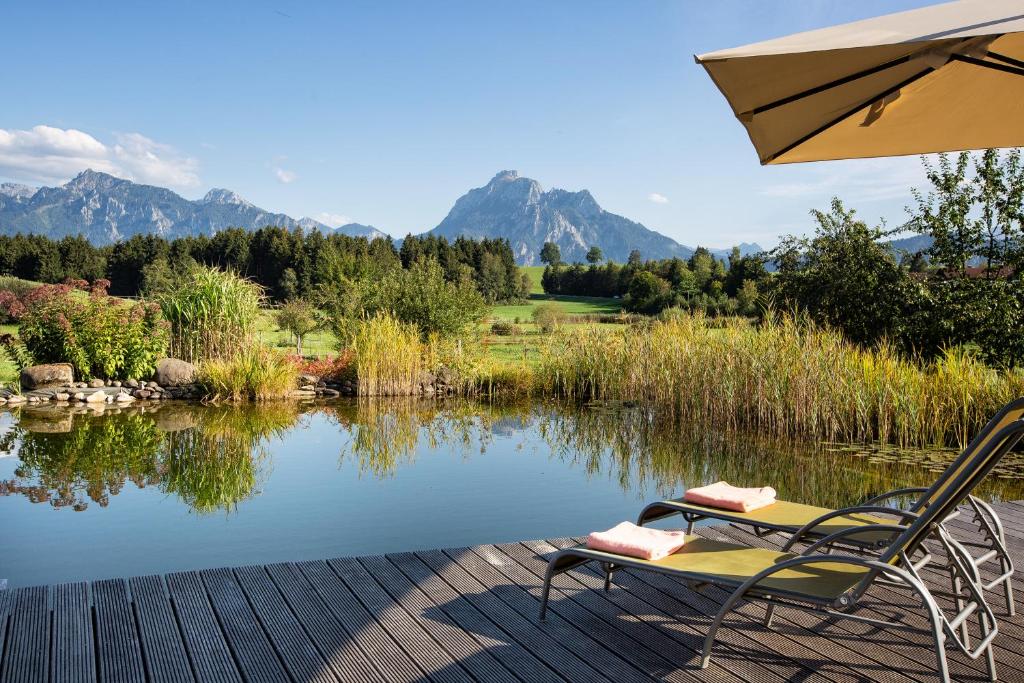einen Stuhl und einen Regenschirm neben einem See in der Unterkunft Landhaus Kössel in Füssen