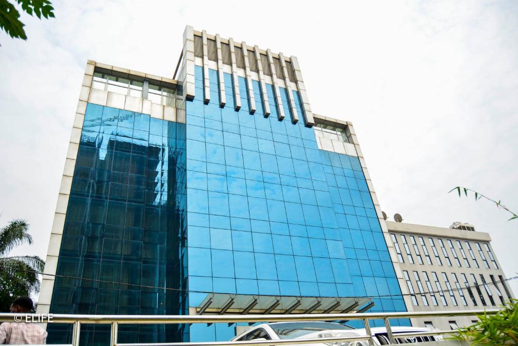 a tall glass building with a car parked in front of it at Hotel Amaritsah in Brazzaville