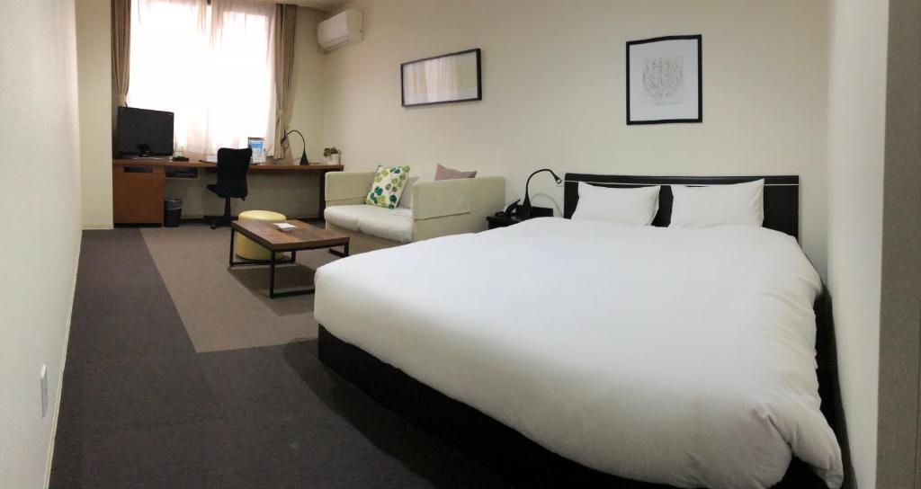 a bedroom with a large white bed and a living room at Hotel Tohkai in Atsugi