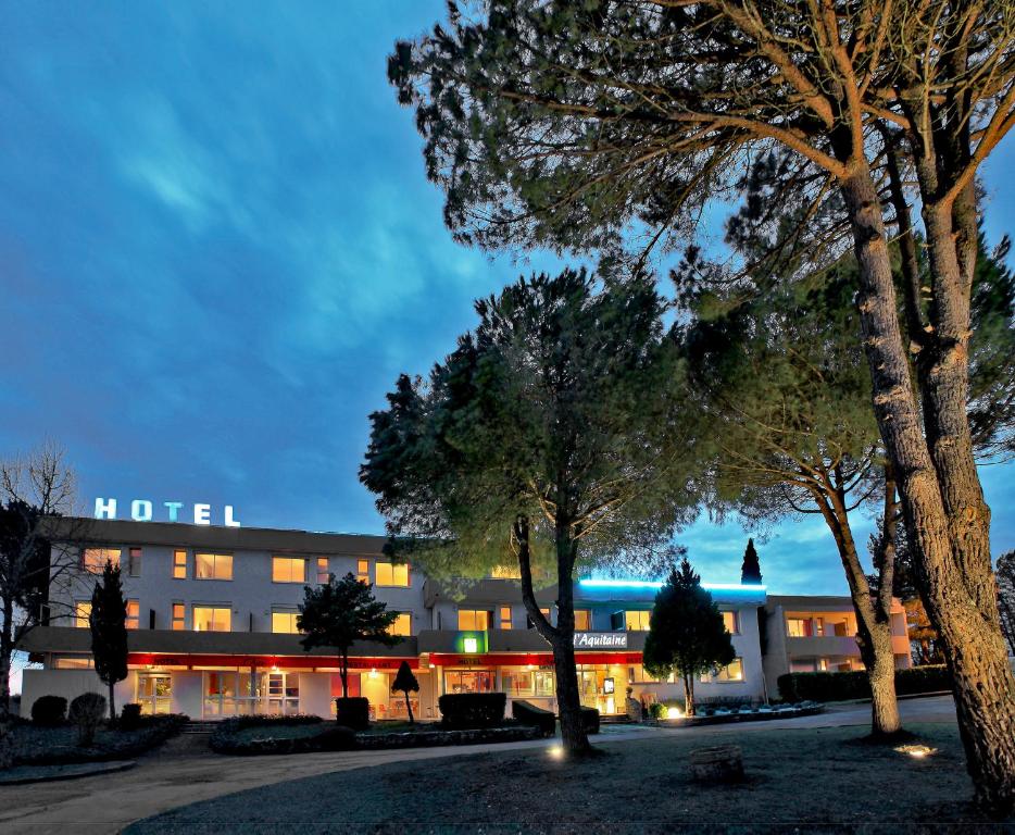 un hôtel la nuit avec des arbres au premier plan dans l'établissement L'Aquitaine - Cahors Sud, à LʼHospitalet