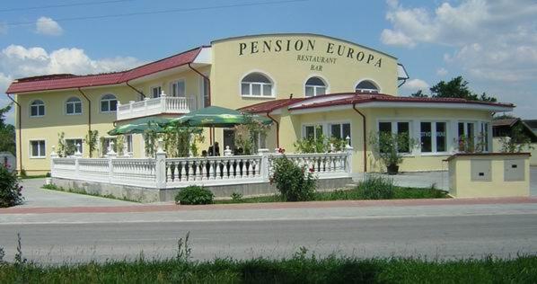 PENZION EUROPA Diakovce في Diakovce: مبنى اصفر امامه سياج ابيض
