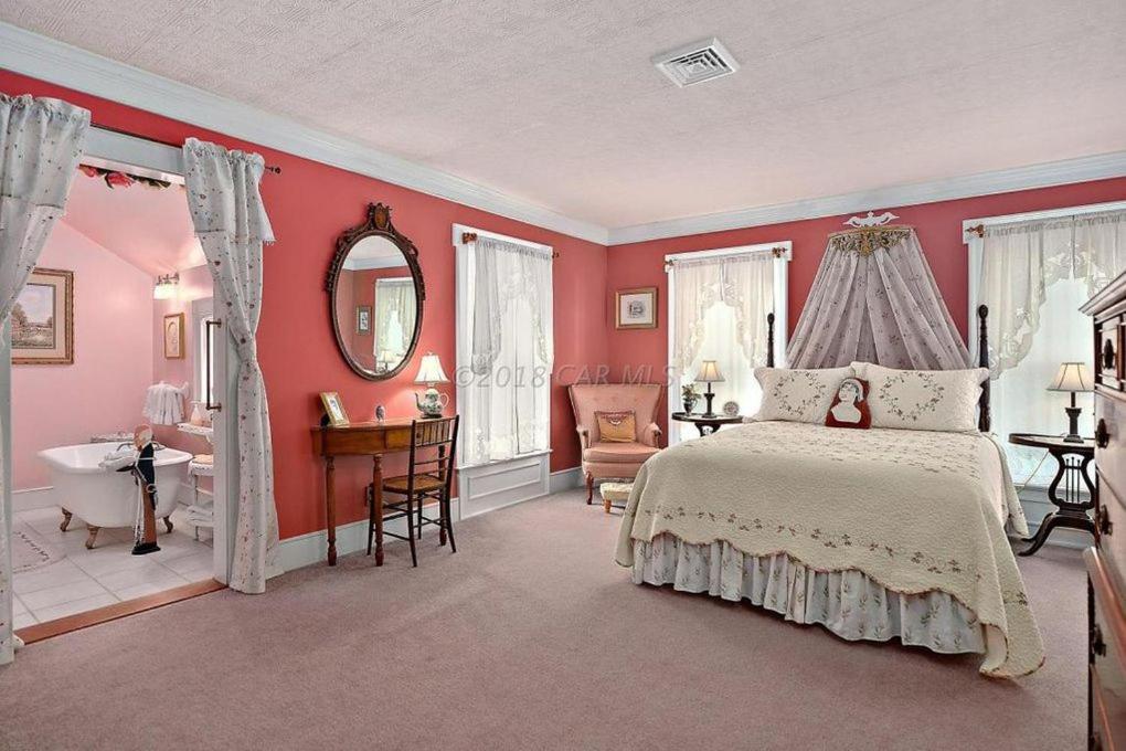 um quarto com paredes cor-de-rosa, uma cama e uma casa de banho em Princess Anne Book Lovers Inn em Princess Anne