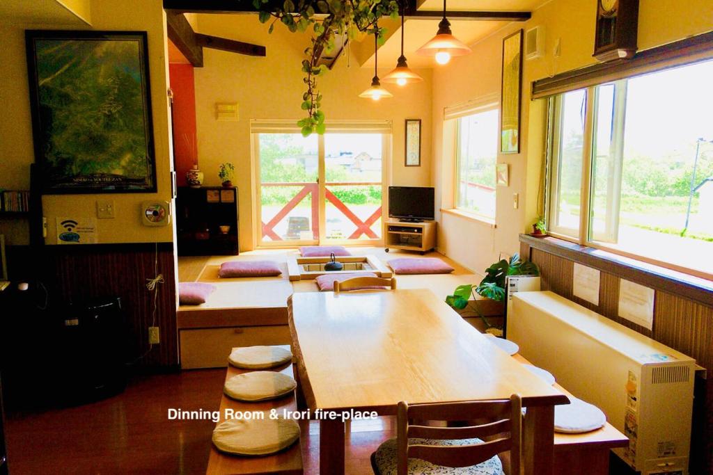 ein Esszimmer mit einem Tisch, Stühlen und Fenstern in der Unterkunft Niseko Tabi-tsumugi Backpackers in Kutchan