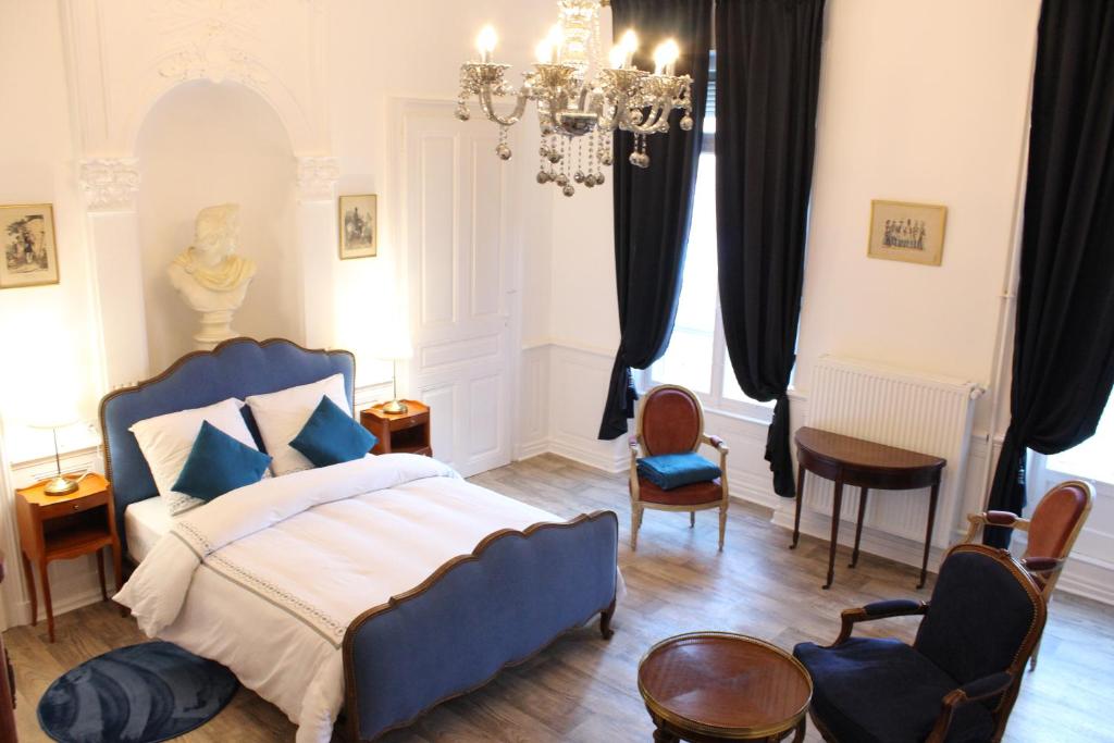 Un dormitorio con una cama y sillas azules y una lámpara de araña. en Le Napoléon, en Luxeuil-les-Bains