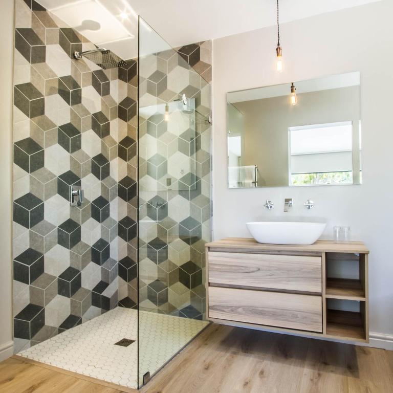a bathroom with a shower with a sink and a mirror at Hlangana Lodge in Oudtshoorn