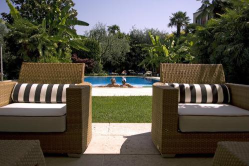 2 sillas de mimbre sentadas junto a una piscina en Hotel 4 Stagioni Sensus Spa, en Bardolino