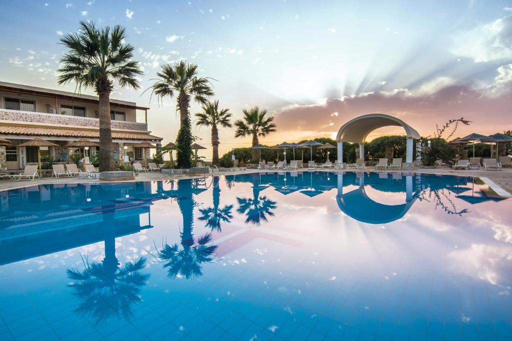 une piscine dans un complexe avec des palmiers et un coucher de soleil dans l'établissement Kouros Palace, à Mastichari