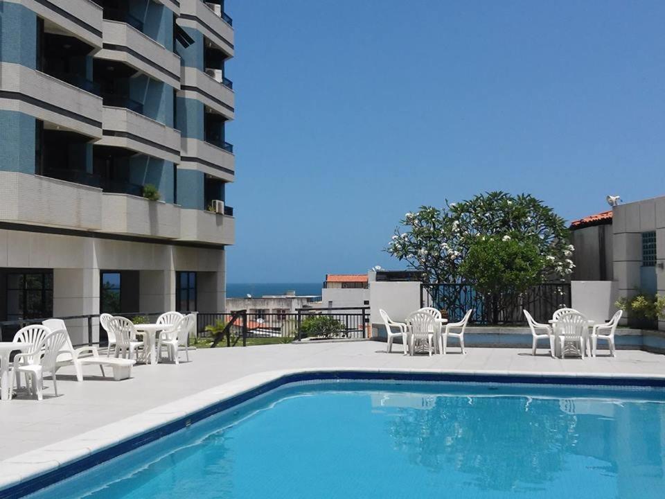 una piscina con sillas blancas y un edificio en Apartamento Barra Tropical Residence, en Salvador