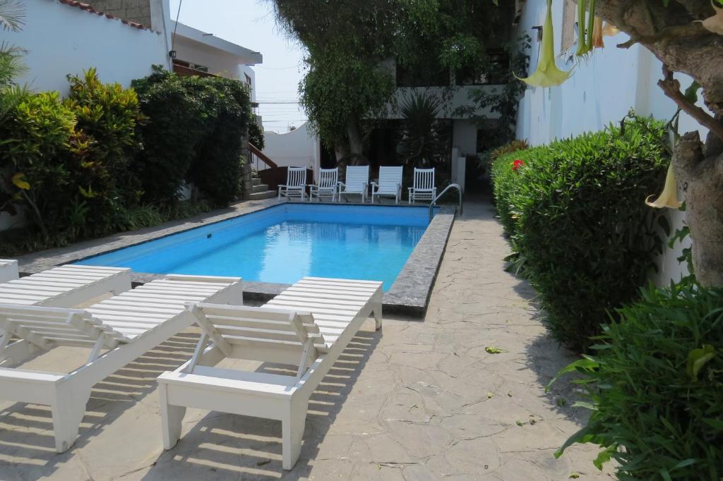 a swimming pool with white lounge chairs and chairs around it at Huanchaco Hostal in Huanchaco
