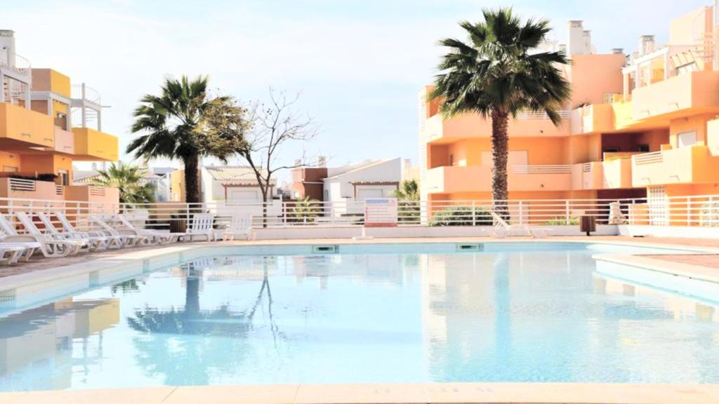 - une piscine avec des chaises, des palmiers et des bâtiments dans l'établissement Terraços Vista Mar Royal Cabanas, à Cabanas de Tavira