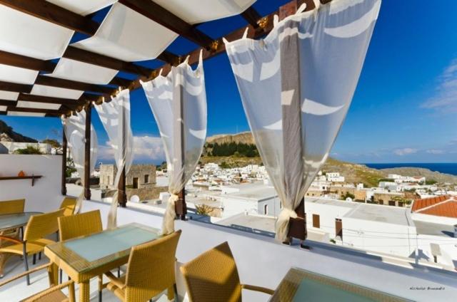 a balcony with tables and chairs and a view of a city at Xenones Lindos in Líndos