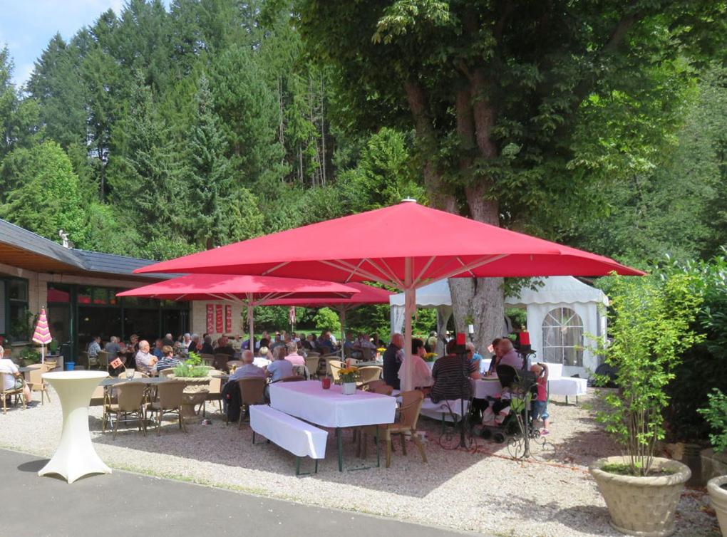 un grupo de personas sentadas en las mesas bajo un paraguas rojo en Diamanthotel Idar-Oberstein, en Idar-Oberstein