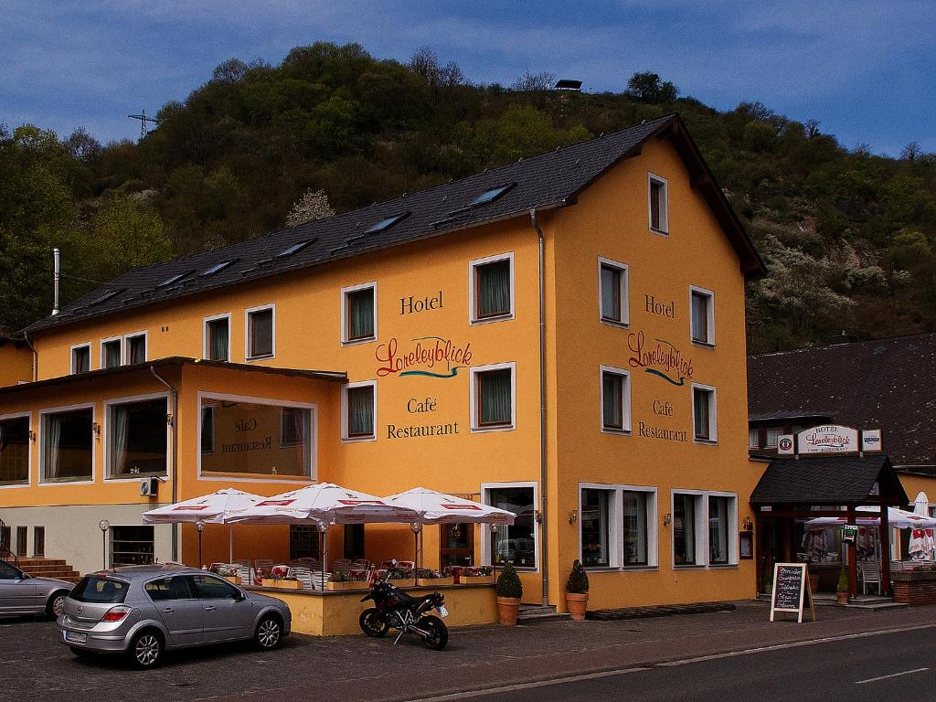 een groot geel gebouw met auto's geparkeerd voor het bij Hotel Cafe Restaurant Loreleyblick in Sankt Goar