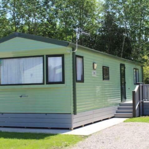 a green tiny house sitting in the grass at Carmels Caravan Borwick Lakes in Carnforth