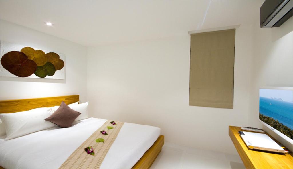 a white bedroom with a bed and a television at Code Samui Hotel in Mae Nam