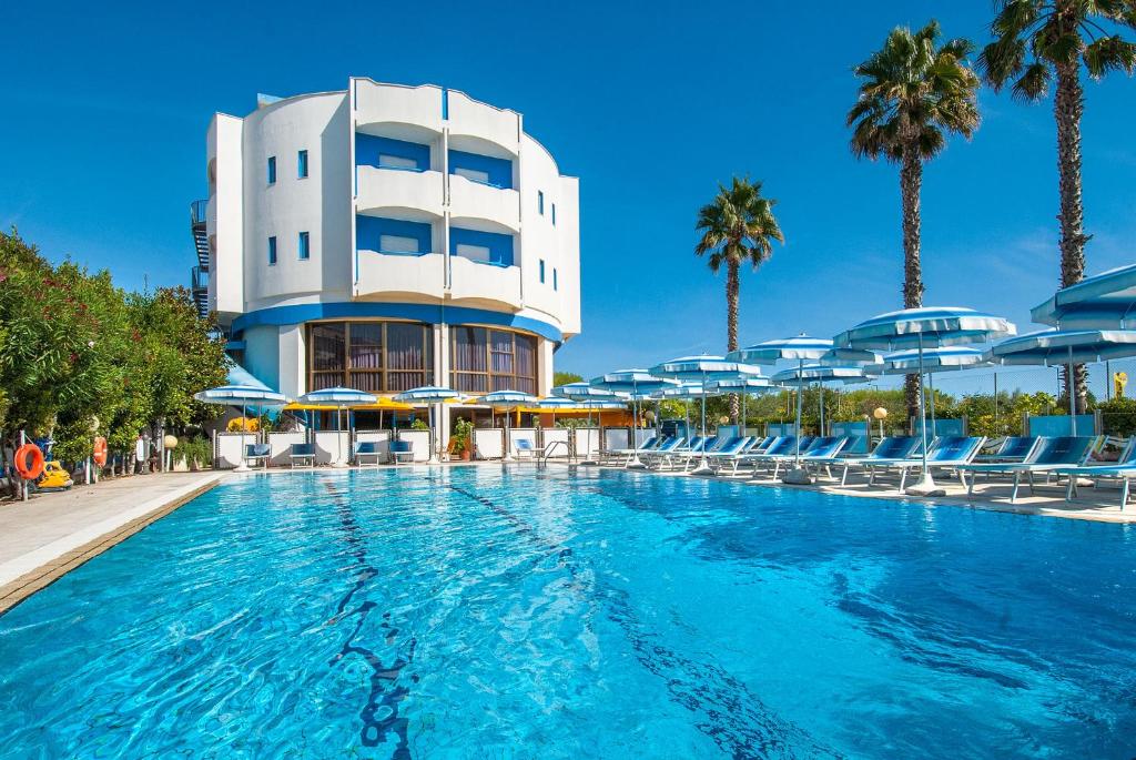 uma piscina em frente a um edifício com palmeiras em Hotel Olimpic em Martinsicuro