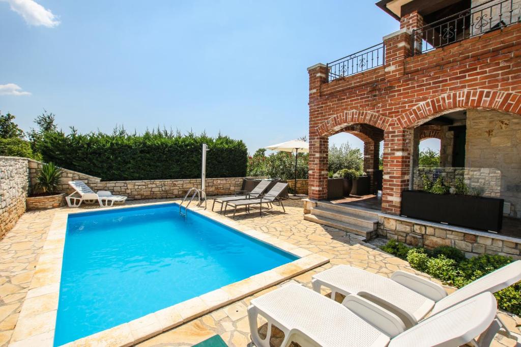 a swimming pool with white chairs and a house at Villa Istriana Jakob with pool in Vabriga