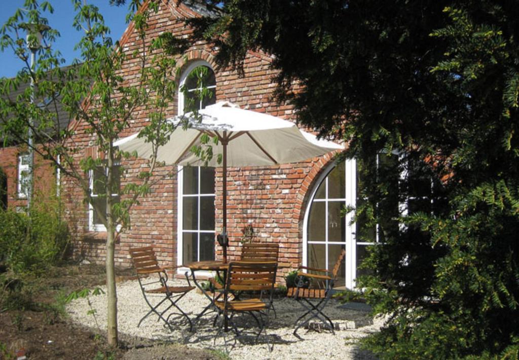 een tafel en stoelen met een parasol voor een bakstenen gebouw bij Upleward Cottage in Krummhörn