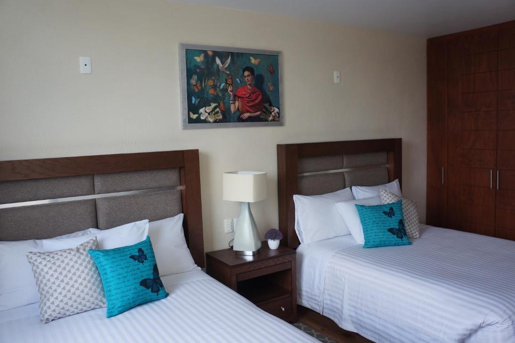 Tlaxcala de XicohténcatlにあるHotel Mirante Tlaxcalaのベッドルーム1室(ベッド2台付)が備わります。壁には絵画が飾られています。