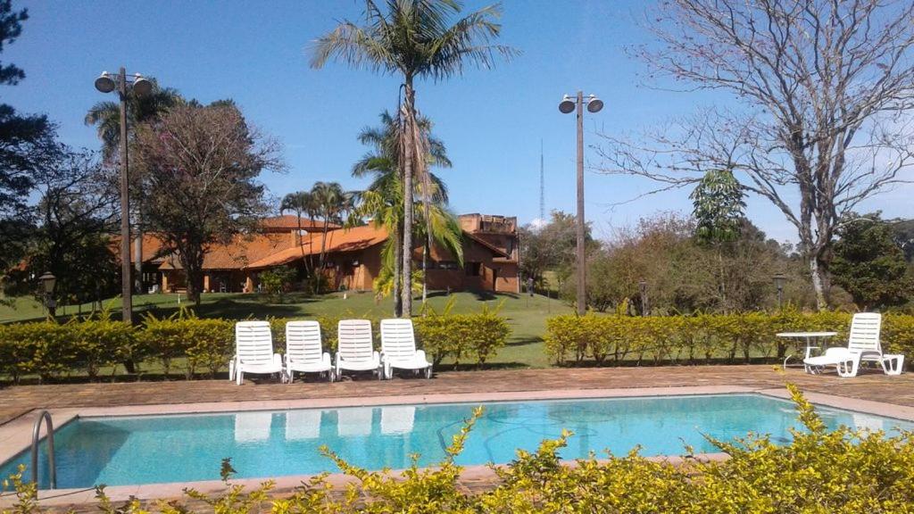 a swimming pool with chairs and a table and a house at Chacara Jequitiba in Itu