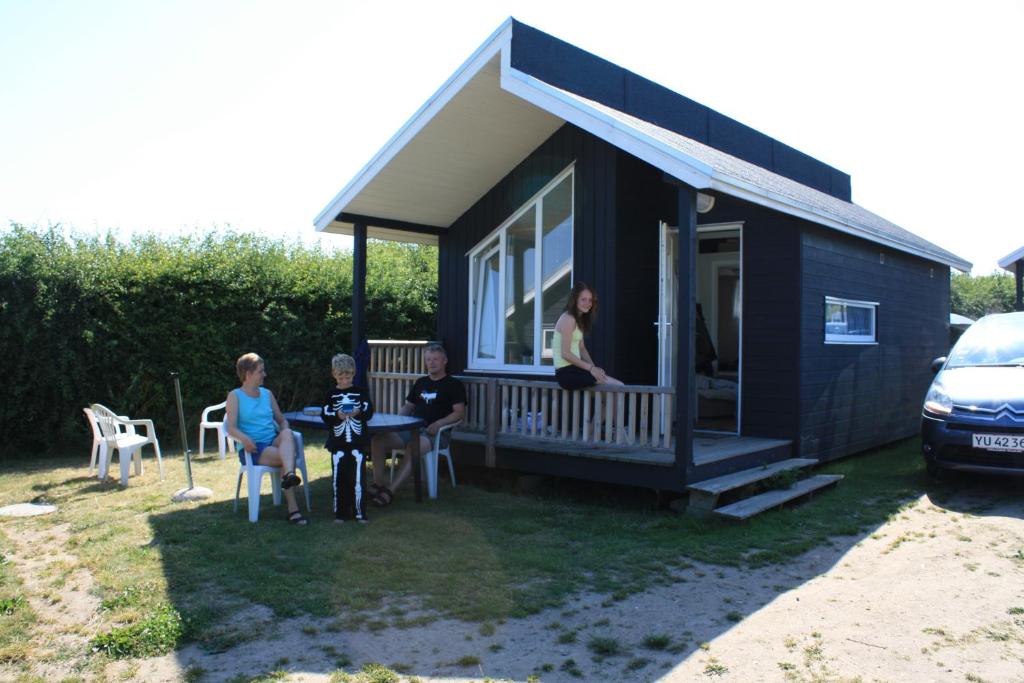 rodzina siedząca na ganku małego domku w obiekcie Vesterlyng Camping and Cottages w mieście Føllenslev