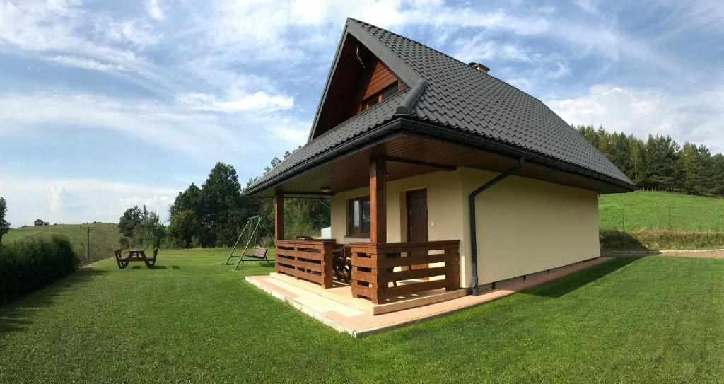 a small house with a black roof on a green field at Domek u Bigola in Polańczyk