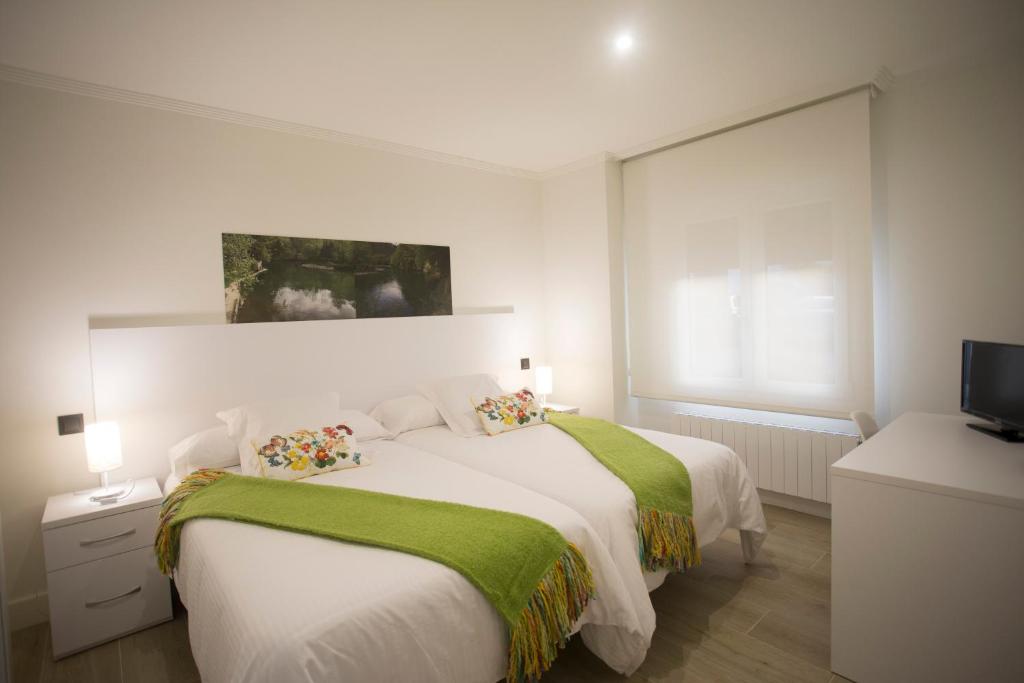 a white bedroom with two beds and a flat screen tv at Canto Encaramado in Gibaja