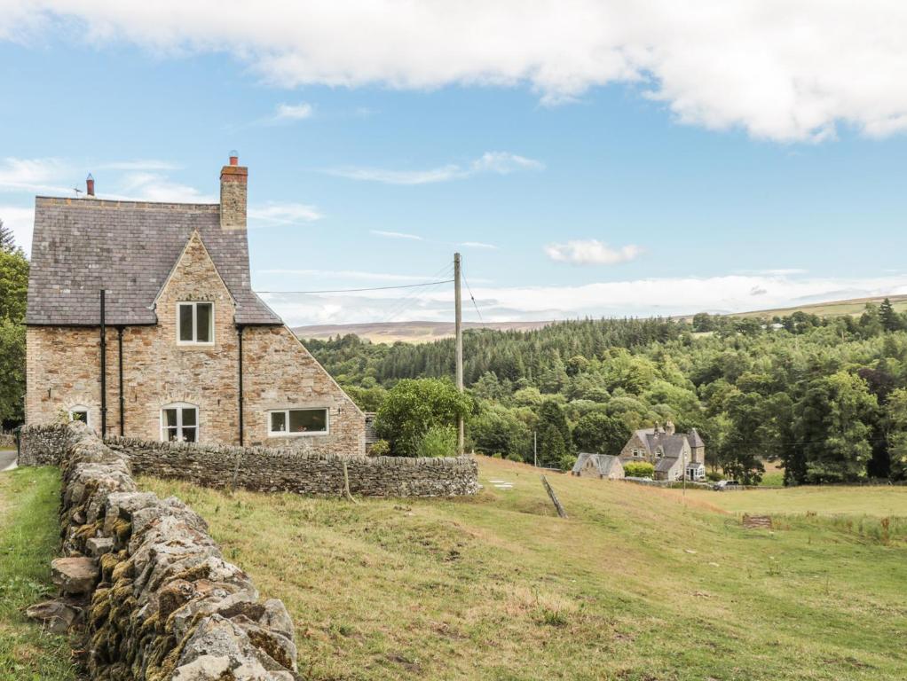 an old stone house on a hill with a stone wall at Newbiggin Cottage in Blanchland